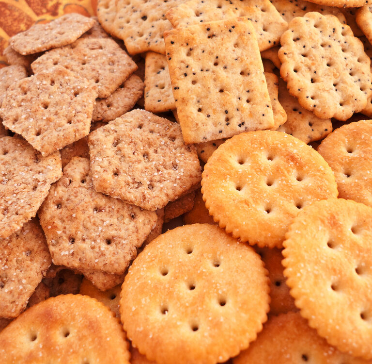 An assortment of crackers, including round, square, and hexagonal shapes, with different textures and grain types, arranged closely together on a patterned surface.