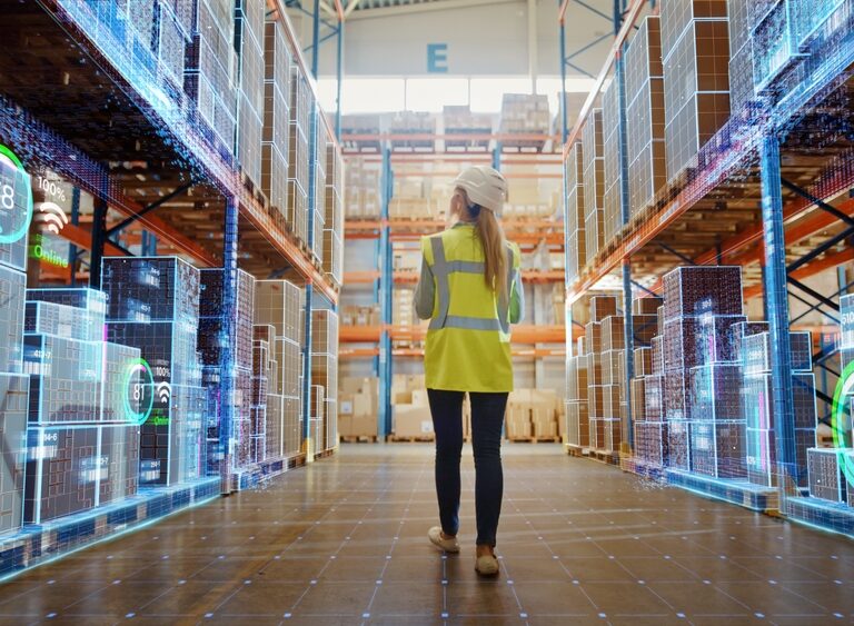 A person in a yellow safety vest and hard hat walks through a warehouse aisle, surrounded by shelves of boxes. Digital graphics display data and analytics overlays, highlighting smart technology powered by Microsoft Fabric for inventory management.