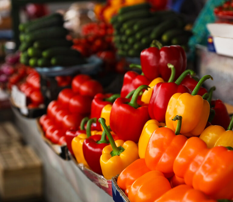 Colorful bell peppers in yellow, orange, and red are stacked on a market stall, arranged as seamlessly as cloud computing organizes data. Other vegetables like cucumbers and tomatoes enhance the vibrant, fresh atmosphere.