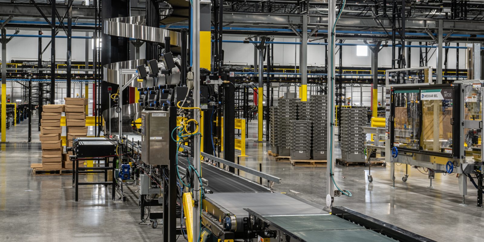 A modern warehouse interior featuring slam solutions, with conveyor belts, stacked cardboard boxes, metal shelves, and various machinery, all under bright industrial lighting.