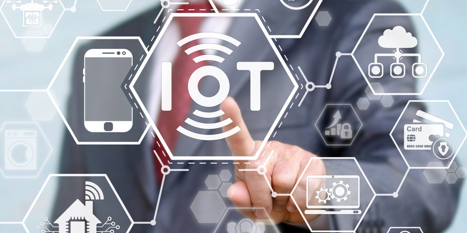 A person in a suit touches a transparent screen with “IoT” at the center, surrounded by icons representing smart devices and technologies, symbolizing the Internet of Things concept.