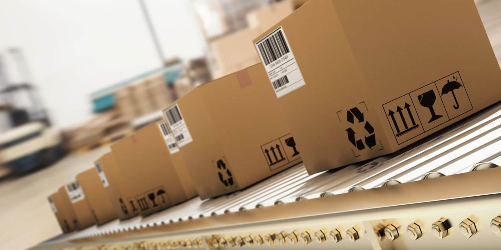 Several cardboard boxes with shipping labels and handling symbols move along a conveyor belt in a warehouse or distribution center. The background is blurred, emphasizing the boxes in the foreground.