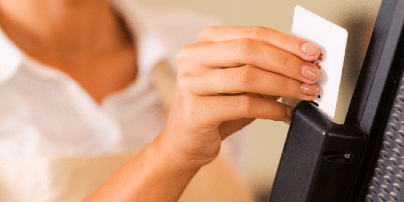 A smiling person in an apron swipes a card through a point-of-sale terminal, suggesting they are processing a payment at a store or café.