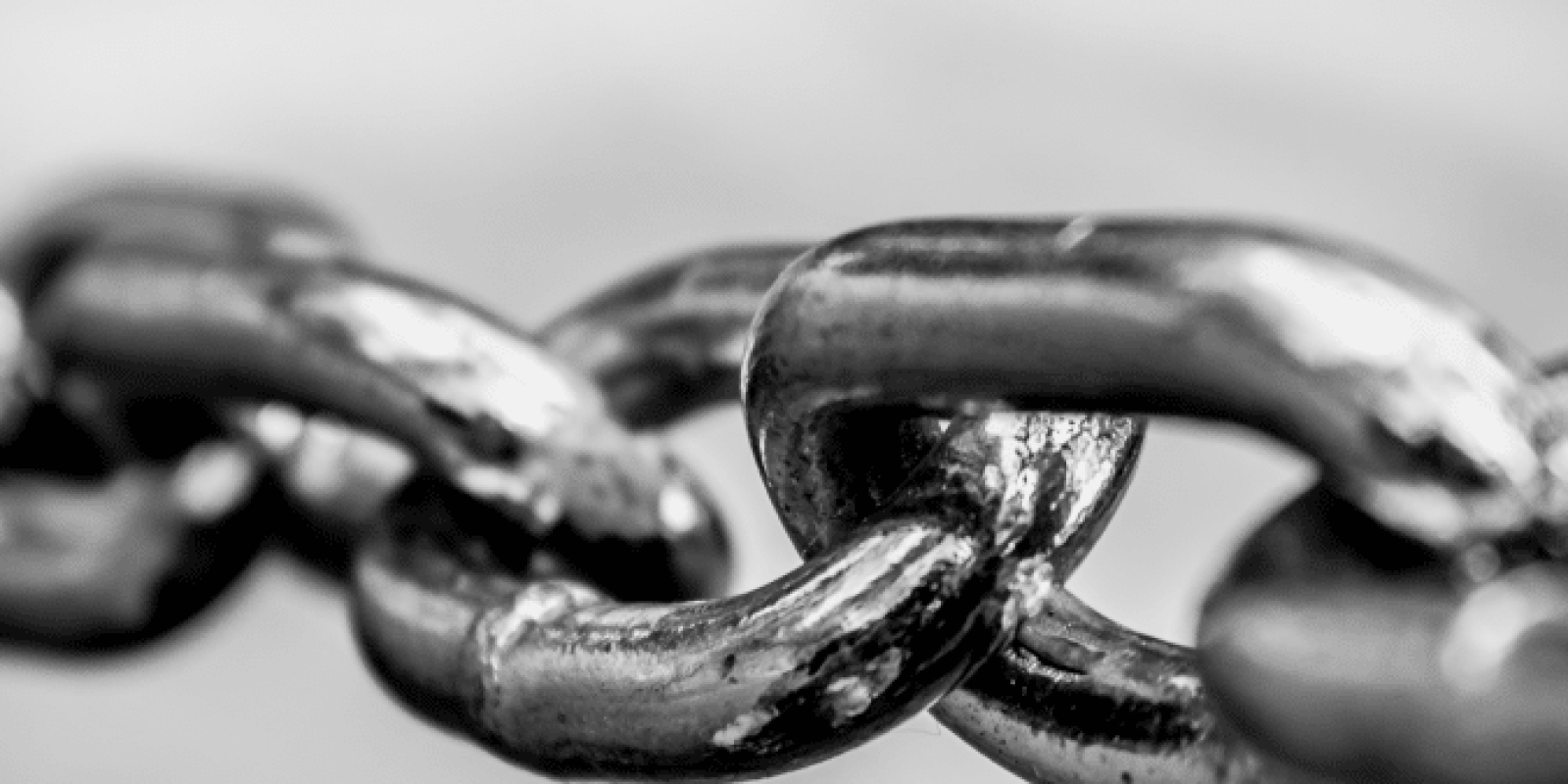Close-up, black and white photo of metal chain links, with one link in sharp focus and the others fading into a blurred background.