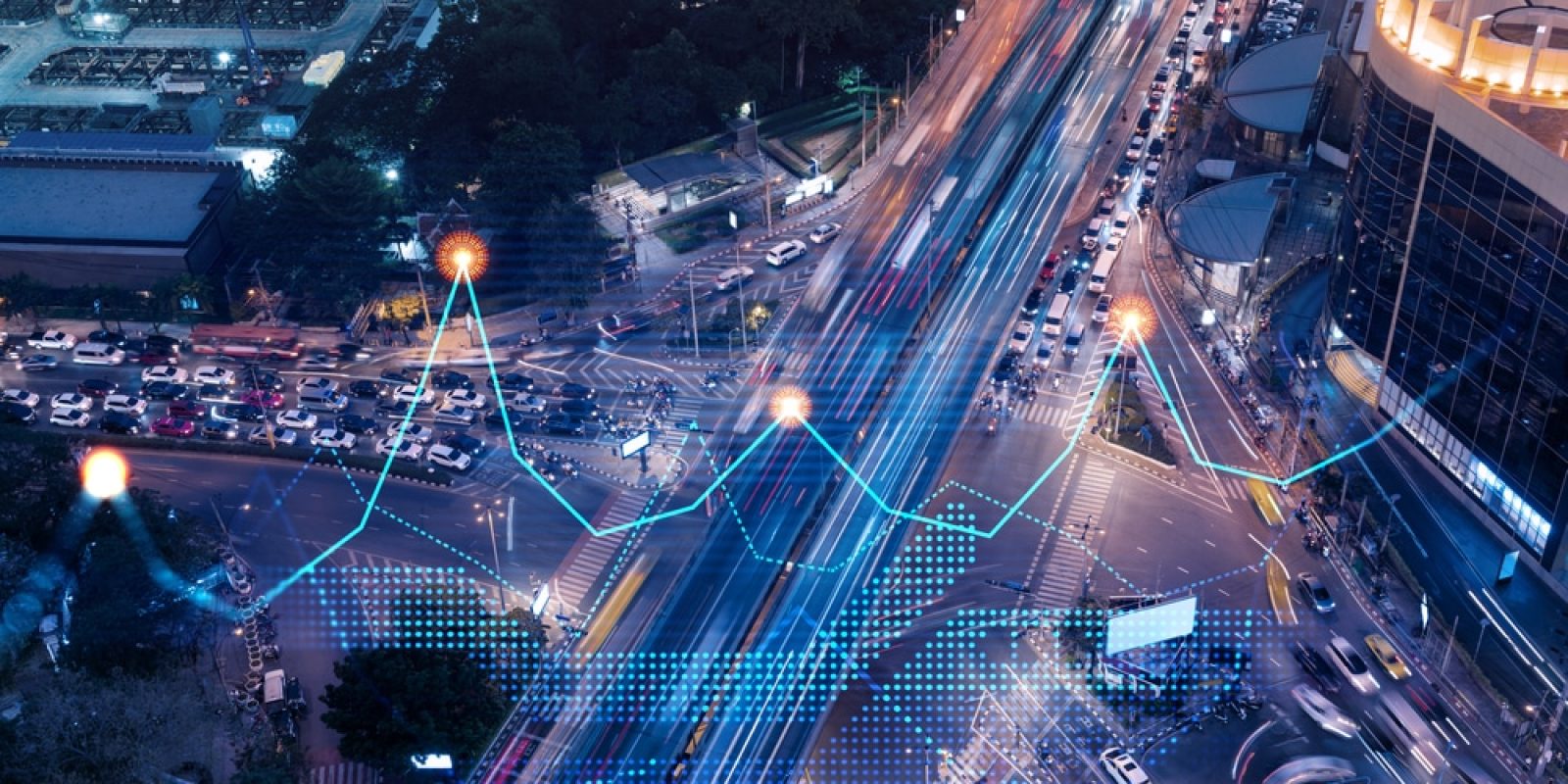 Aerial view of a busy city intersection at night with light trails from traffic. Overlaid graphics show data points, lines, and digital grids, representing data analysis or smart city technology.