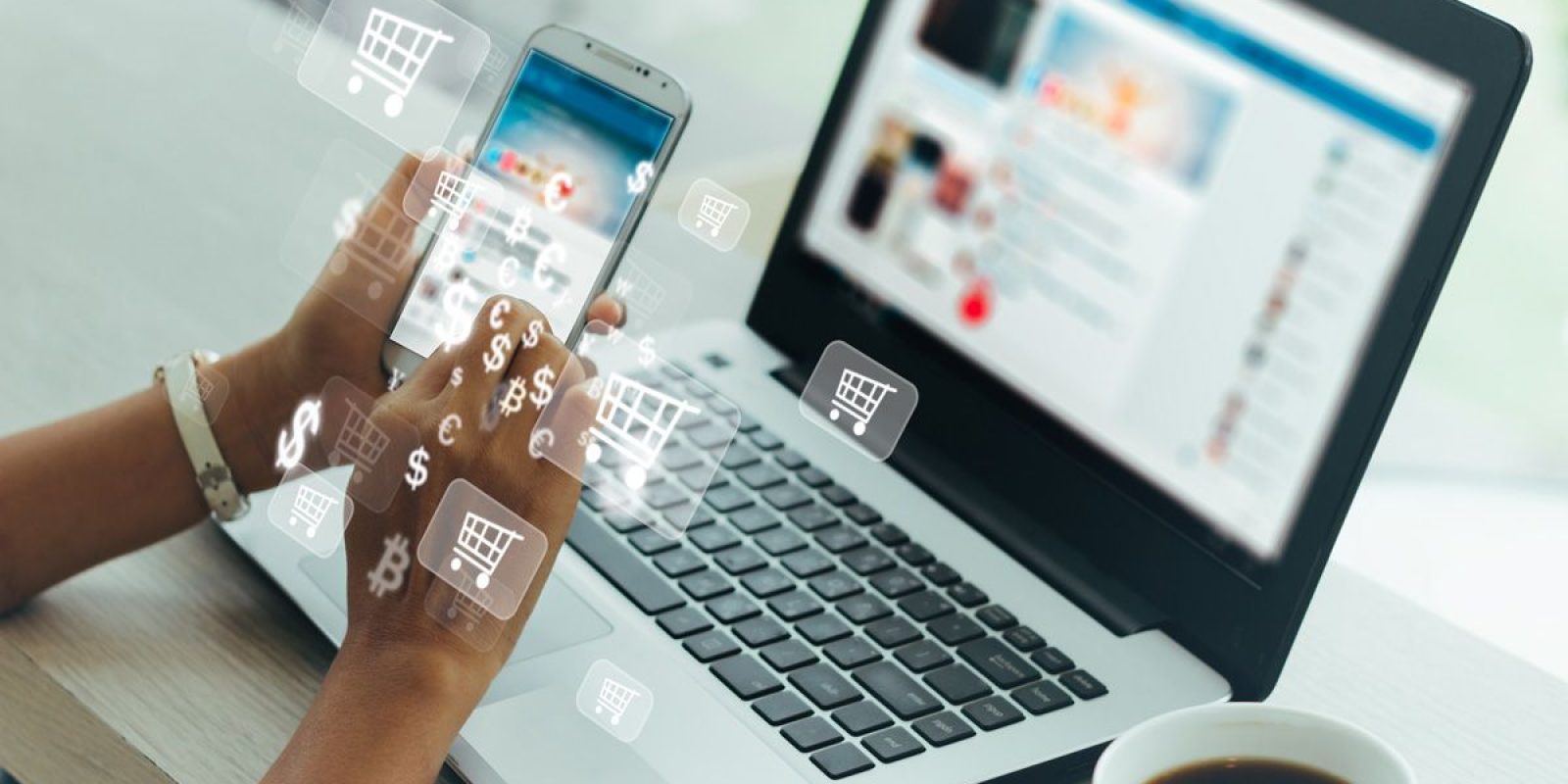 A person uses a smartphone and laptop simultaneously at a table with a coffee cup, with digital shopping cart, dollar, and currency symbols overlaying the image, representing online shopping or e-commerce.