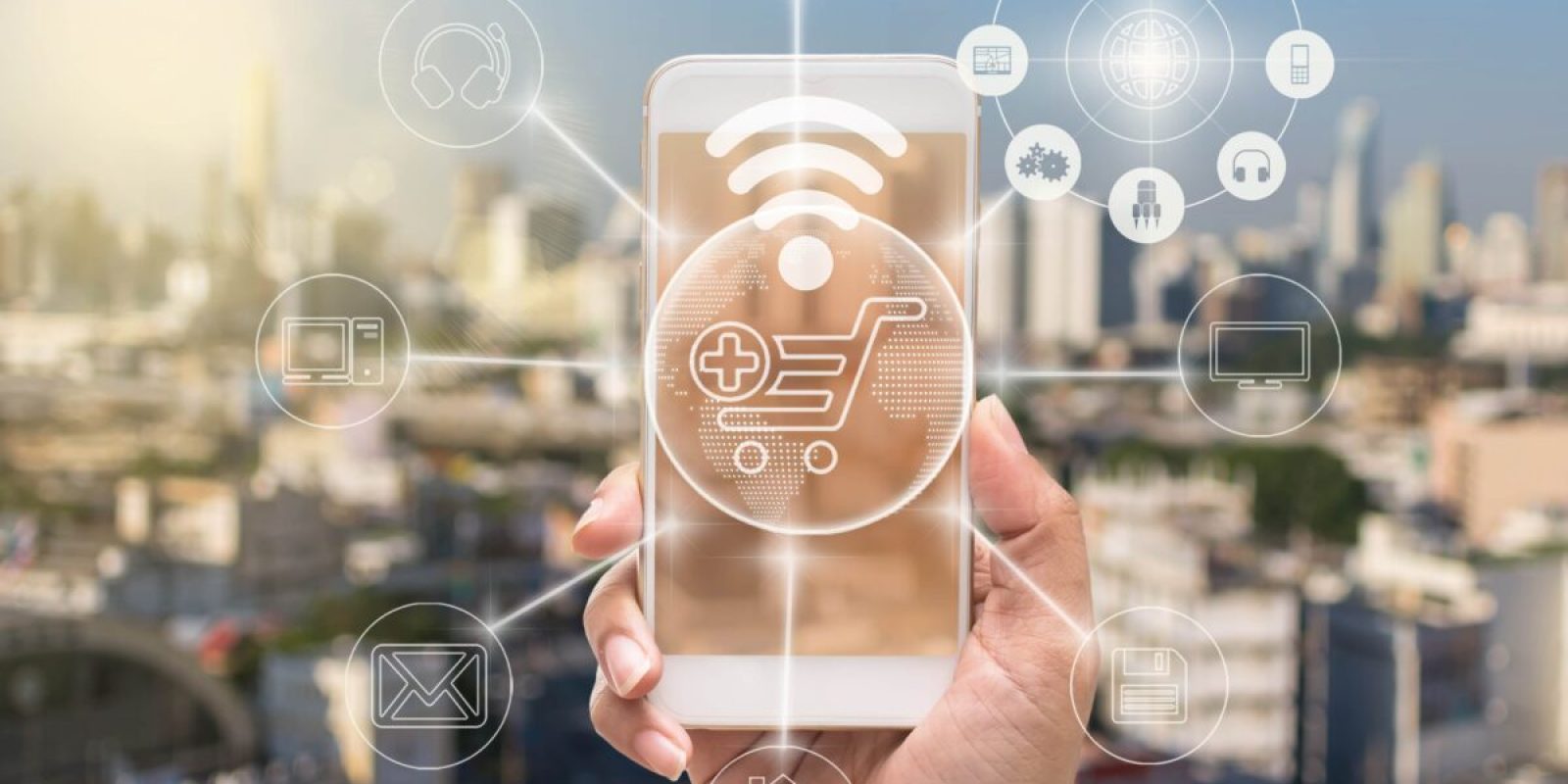A hand holds a smartphone with a glowing shopping cart icon and digital network symbols, representing online shopping, order management systems, and connectivity against a blurred cityscape background.
