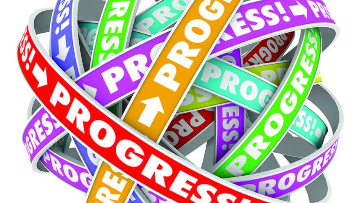 A tangled ball of colorful ribbons with the word “PROGRESS!” and arrows printed on each in various colors, symbolizing movement, advancement, and complexity.