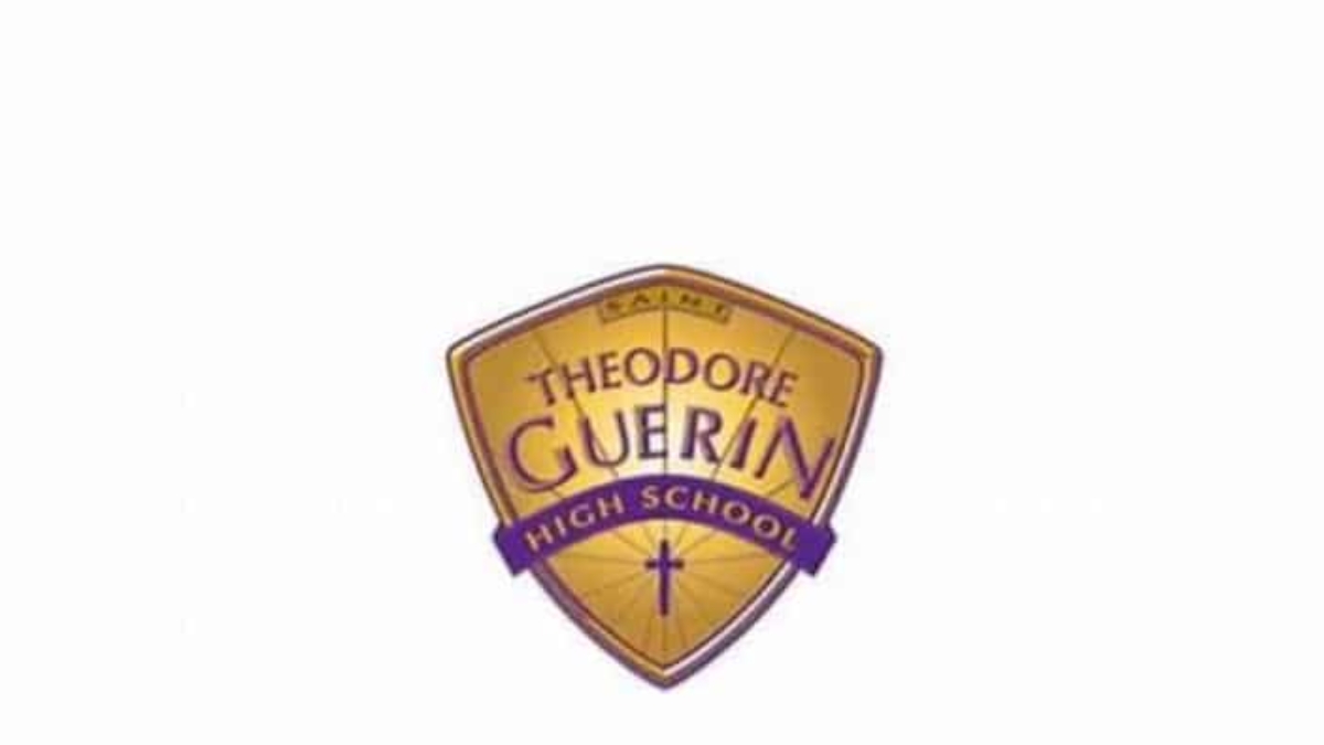 A gold and purple shield logo for Theodore Guerin High School, with the word Saints at the top and a cross at the bottom.
