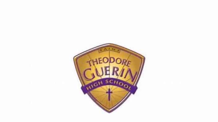 A gold and purple shield logo for Theodore Guerin High School, with the word Saints at the top and a cross at the bottom.