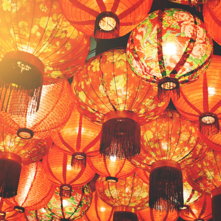 A collection of red paper lanterns with floral patterns hanging closely together, illuminated with warm light, creating a festive and vibrant atmosphere.