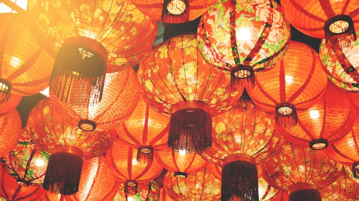 A collection of red paper lanterns with floral patterns hanging closely together, illuminated with warm light, creating a festive and vibrant atmosphere.