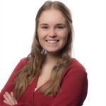 A young woman with long, light brown hair smiles confidently with arms crossed, wearing a red sweater over a white top, against a plain white background.