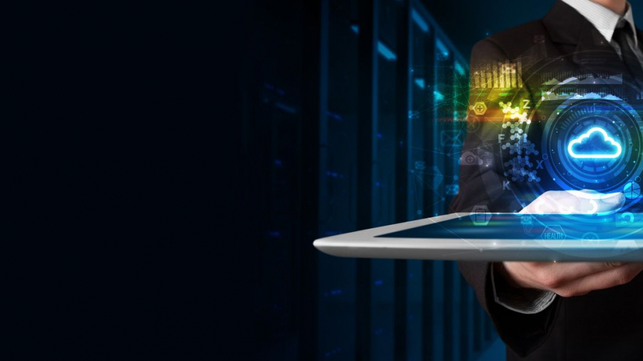 A person in a suit holding a tablet with a glowing cloud computing icon and digital data graphics hovering above it, symbolizing cloud technology and data management, with a dark server room background.