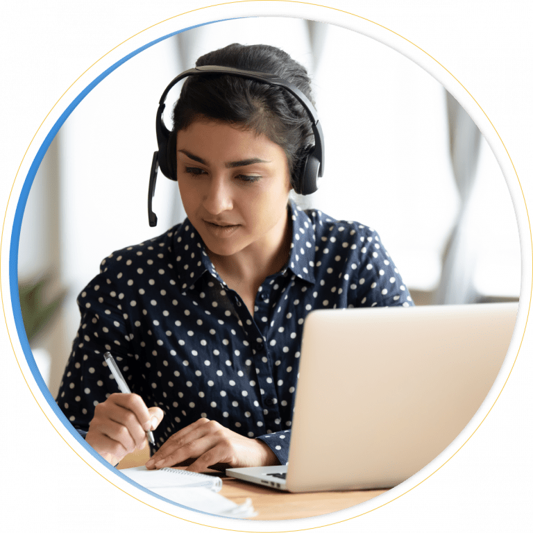 A woman wearing a headset is sitting at a desk, looking at her laptop, and taking notes with a pen on paper. She appears to be engaged in an online Dynamics 365 Customer Service meeting or virtual learning session.