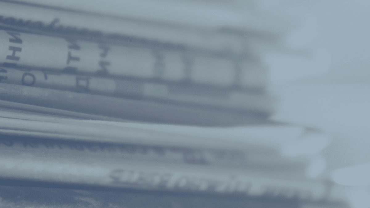 A close-up view of a stack of newspapers, with printed text visible on the pages. The image has a blue tint and a blurred background.