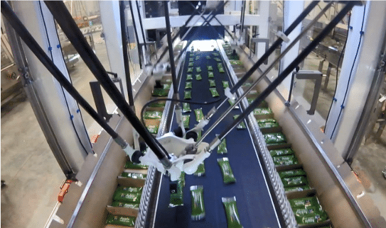 Overhead view of an automated robotic arm sorting green rectangular packages on a conveyor belt inside a large industrial facility.