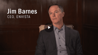 A man in a suit sits for an interview in front of a dark wooden background. On the left, text reads Jim Barnes, CEO, EnVista.