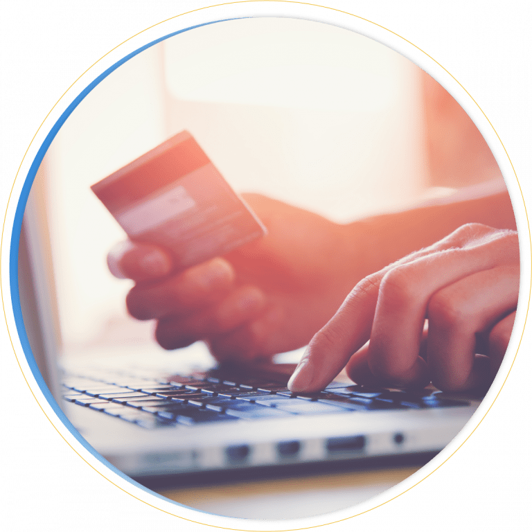 A person holds a credit card in one hand while typing on a laptop keyboard with the other, suggesting an online payment or shopping activity powered by Dynamics 365 Commerce in soft, warm lighting.