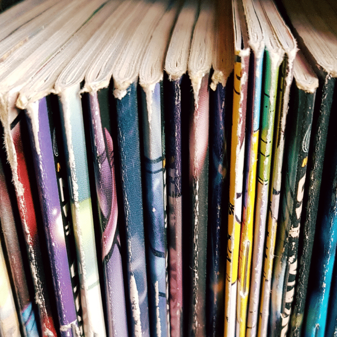 Close-up view of the top edges and spines of several colorful comic books or graphic novels lined up vertically on a shelf.