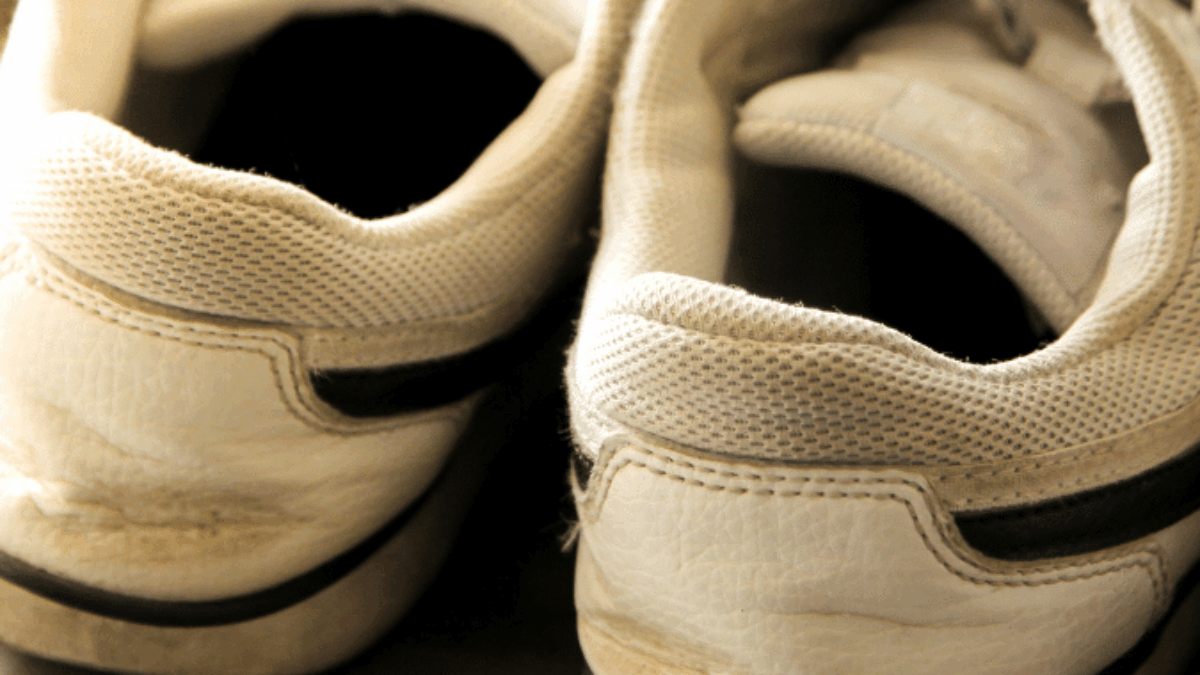 A close-up of the back of a pair of worn white sneakers with dark stripes, resting side by side on a surface. The shoes show signs of use, with creases and slight dirt marks visible.