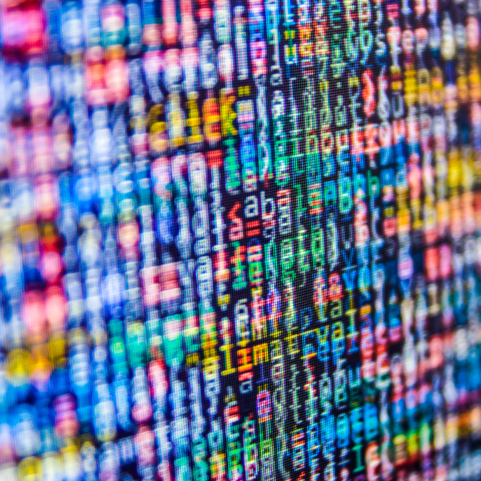 A close-up of a computer screen displaying colorful, blurred lines of programming code in various colors, including blue, green, red, and yellow, creating an abstract, pixelated effect.