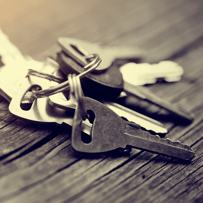 A close-up of several metal keys on a keyring resting on a wooden surface, with a soft focus and warm lighting.