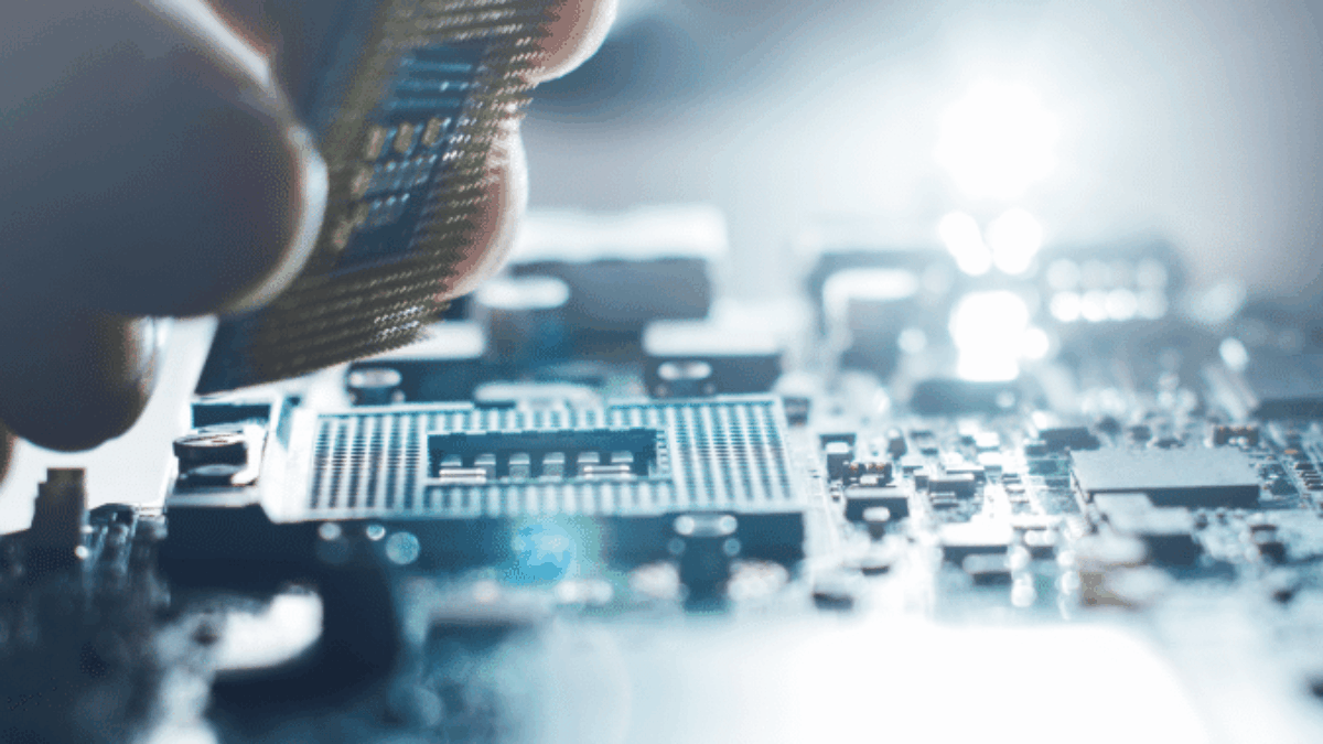 A close-up of a hand installing a computer processor chip onto a motherboard, with a bright light illuminating the electronic components in the background.