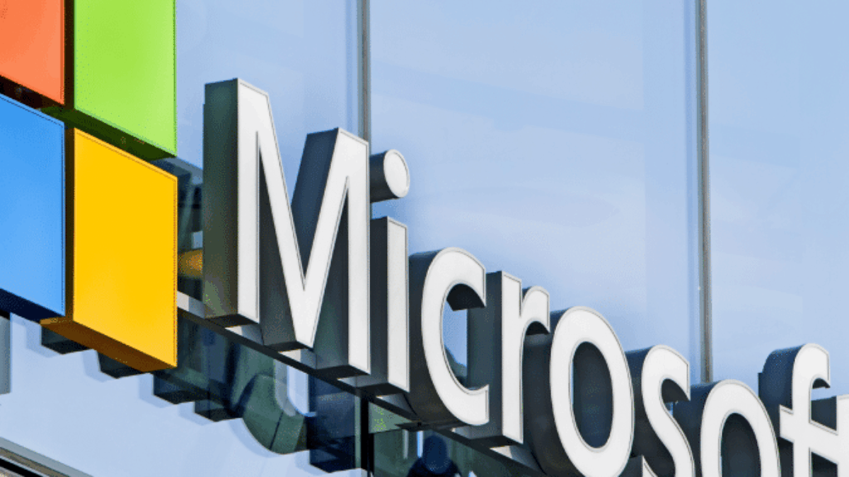 The Microsoft logo, featuring four colored squares and the word Microsoft in large white letters, is displayed on the exterior of a modern glass building.