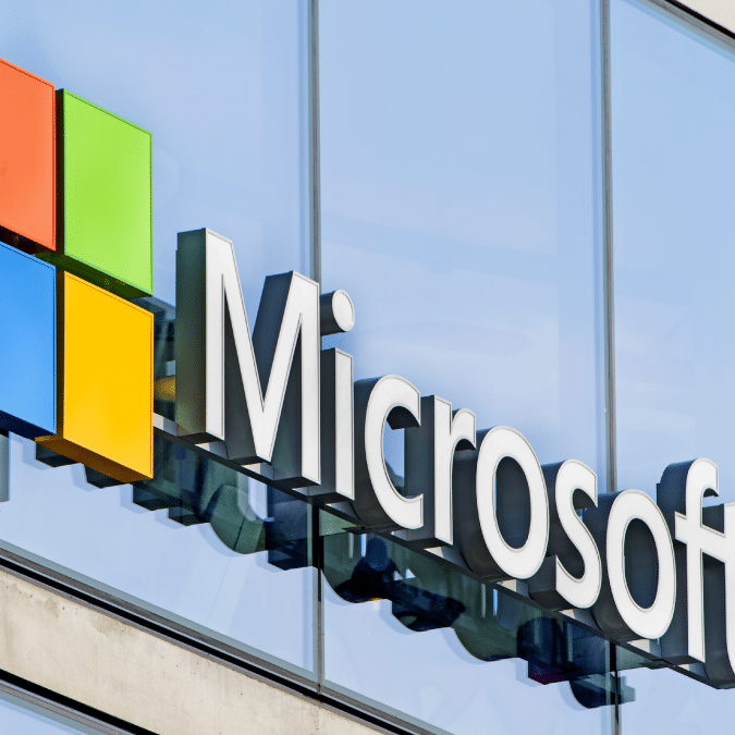 The Microsoft logo, featuring four colored squares and the word Microsoft in large white letters, is displayed on the exterior of a modern glass building.