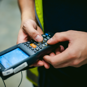 A person in a high-visibility vest operates a handheld barcode scanner, highlighting their hands and device—an essential tool during WMS implementation for efficient inventory management.
