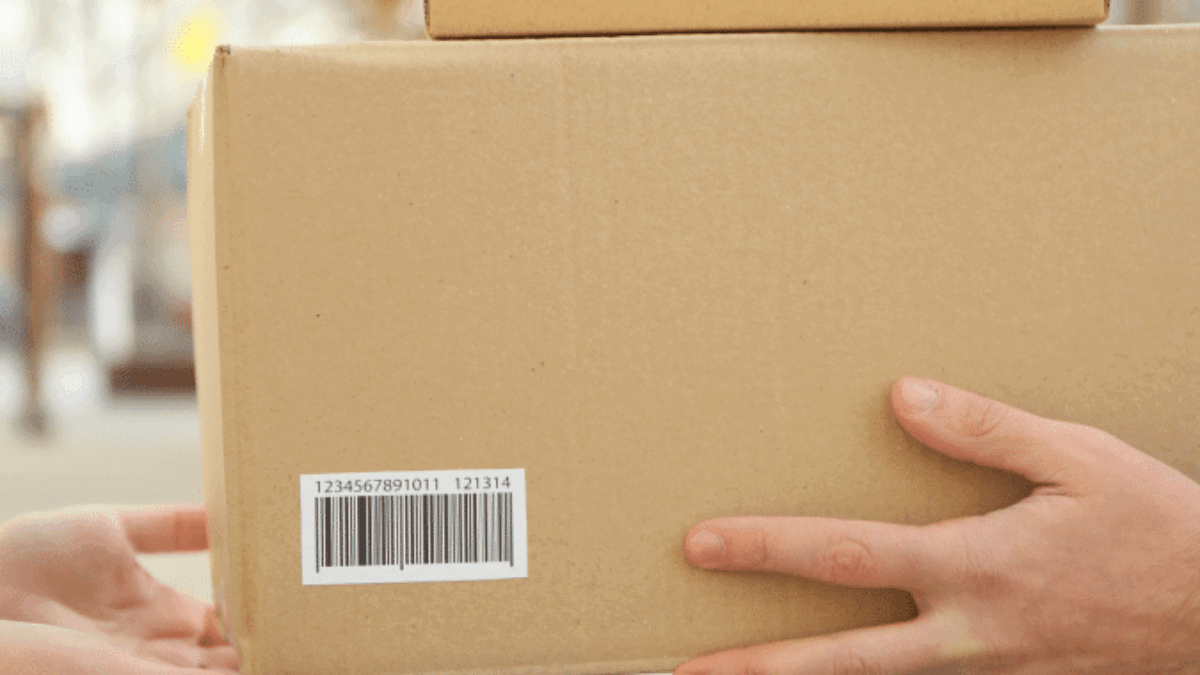 Two hands exchange two cardboard boxes with barcodes outdoors, one person handing the boxes to the other.
