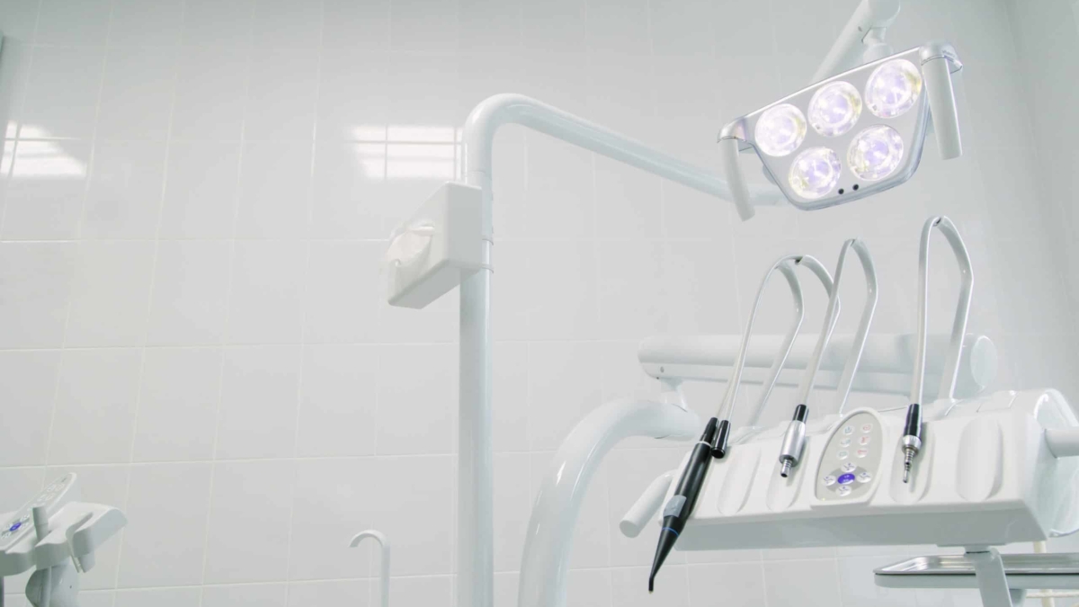 Modern dental office with bright overhead lights, dental instruments, and a clean white tiled wall, showcasing a sterile and organized environment for dental procedures.