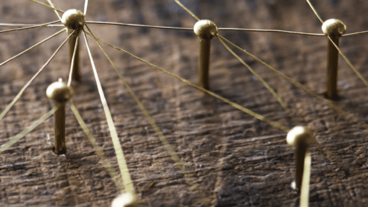 Close-up of gold pins connected by thin strings on a wooden surface, forming a network pattern symbolizing connections, communication, or a web of relationships.