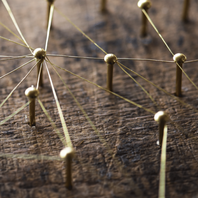 Close-up of gold pins connected by thin strings on a wooden surface, forming a network pattern symbolizing connections, communication, or a web of relationships.