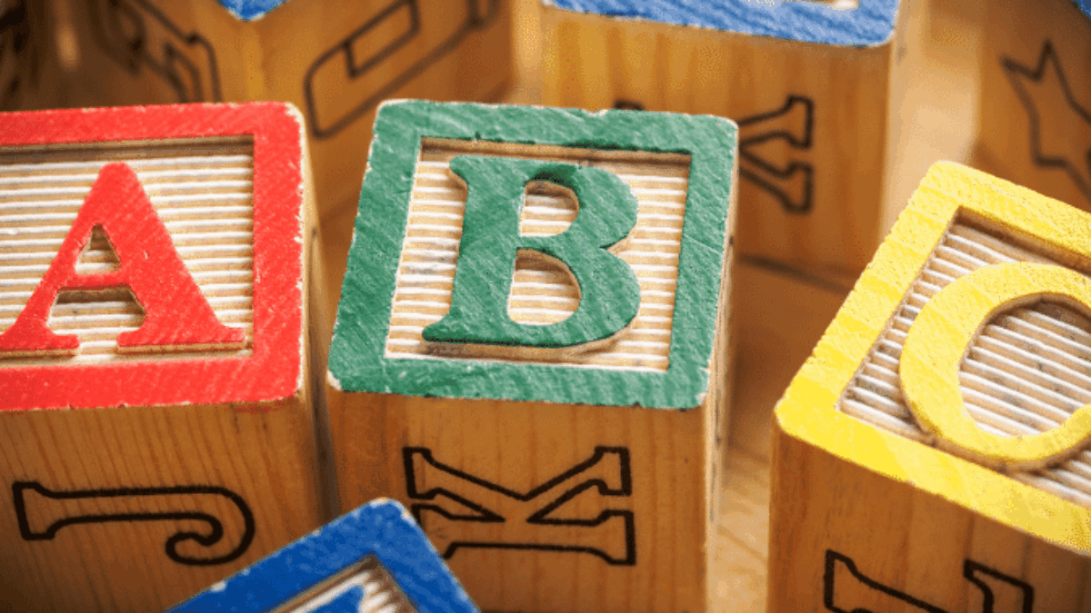 Colorful wooden alphabet blocks are arranged closely together, with the letters A, B, and D most prominently visible on the blocks faces. The blocks have textured surfaces and painted borders in red, green, blue, and yellow.