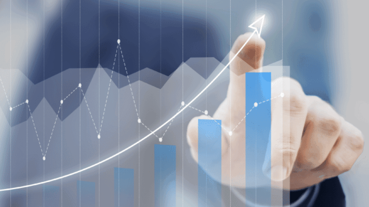 A person in a suit points at a growing bar graph with a rising trend line, symbolizing business growth or financial success. The background is blurred to emphasize the chart.