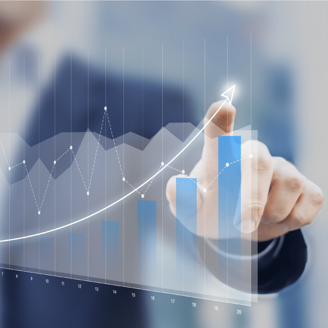 A person in a suit points at a growing bar graph with a rising trend line, symbolizing business growth or financial success. The background is blurred to emphasize the chart.