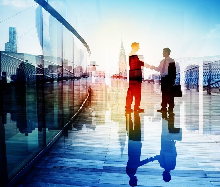 Two businesspeople shake hands on a modern glass walkway, with a city skyline and tall buildings visible in the background, and their reflections on the shiny floor.