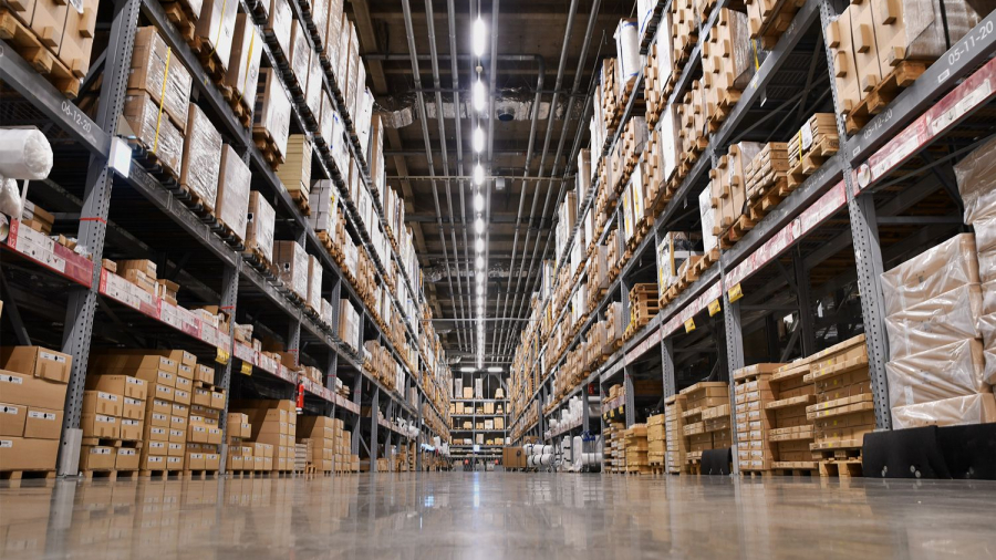 View of a large warehouse with tall shelves stacked with cardboard boxes, ideal for warehouse capacity analysis, bright overhead lighting, and a shiny concrete floor, seen from a low angle between the aisles.