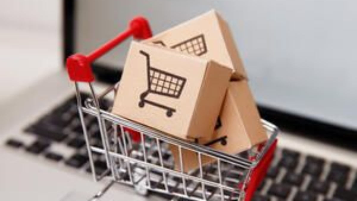 A miniature shopping cart holds small cardboard boxes with shopping cart icons, placed on a laptop keyboard, symbolizing online shopping or e-commerce.