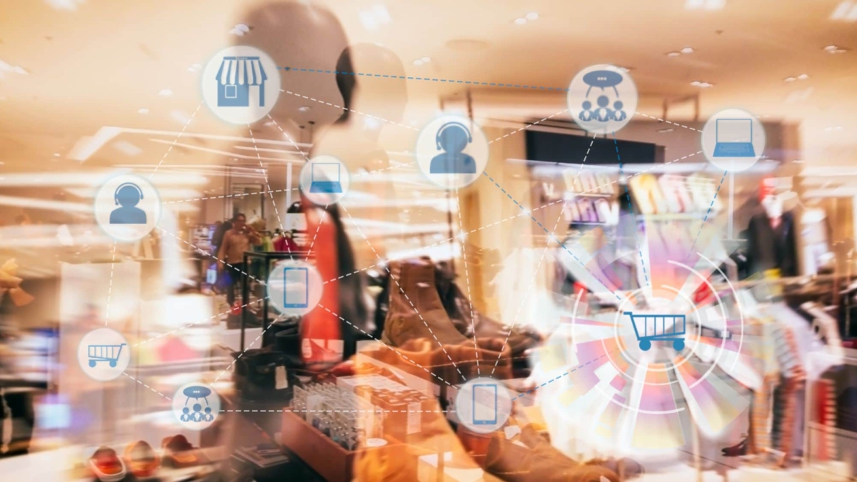 A blurred clothing store interior with digital icons—shopping cart, store, smartphone, and people—connected by lines to represent online shopping, digital retail technology, and enhanced inventory visibility.