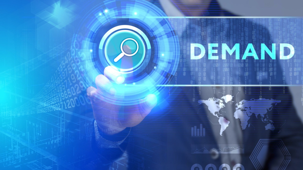 A person in a suit touches a digital search icon on a virtual interface, with the word DEMAND and graphics of data, world maps, and technology in the background.