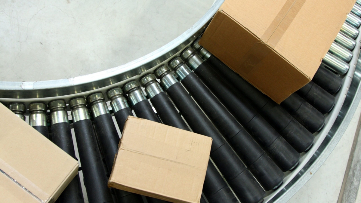 Three cardboard boxes on a curved conveyor belt with black rollers in an industrial setting.