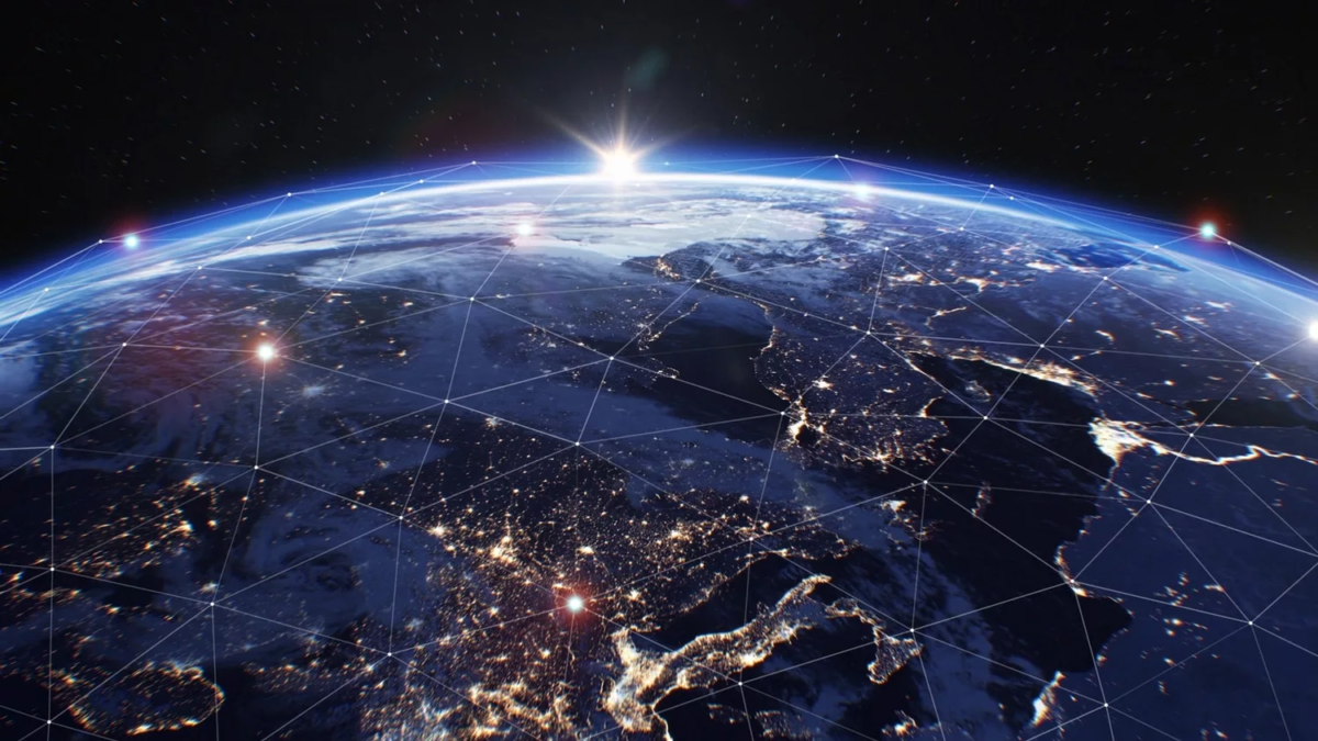 View of Earth from space at sunrise, with illuminated cities and network lines showing global connectivity. The horizon glows with sunlight, and the planets surface features continents and scattered clouds.