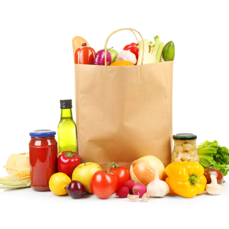 A paper grocery bag filled with fresh vegetables and bread sits on a white background, surrounded by produce like tomatoes and onions—ideal for showcasing effective distribution consulting in food retail.