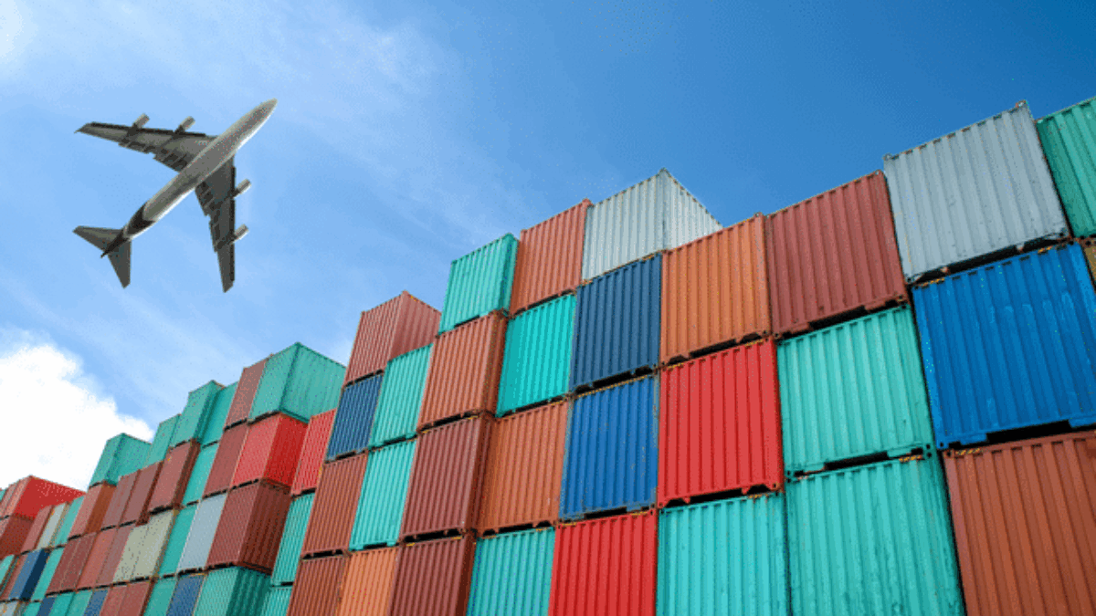 A commercial airplane flies above a large stack of colorful shipping containers under a clear blue sky, symbolizing global trade and transportation logistics.