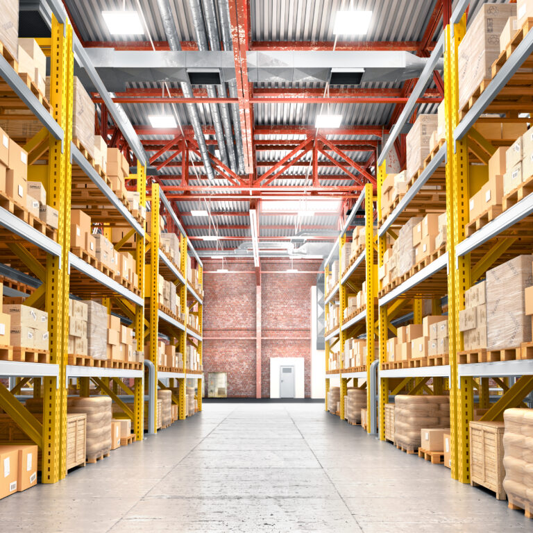 A spacious warehouse with tall shelves filled with cardboard boxes and packages. Robotics integration streamlines operations, while organized rows and a clear concrete floor create an orderly environment brightly illuminated throughout.