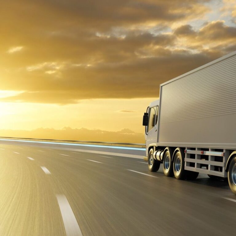 A large white semi-truck drives on a curved highway at sunset, with golden sunlight illuminating the sky and clouds, creating a dramatic and serene atmosphere.