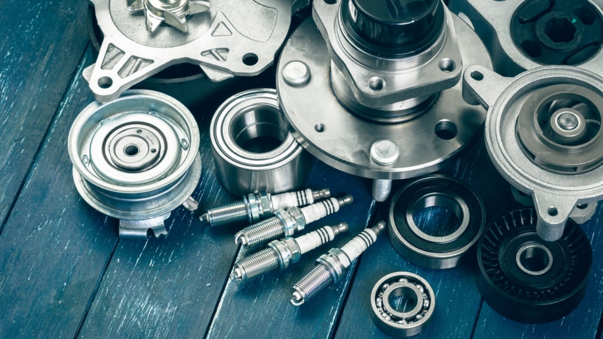 Various metal car engine parts, including spark plugs, bearings, and gears, are arranged on a blue wooden surface. The image highlights the details and textures of the automotive components.